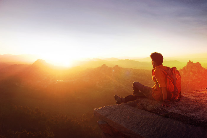 A photo of a backpacker sitting on the edge of a cliff looking toward the sunset. Tips for Light Meter Photography